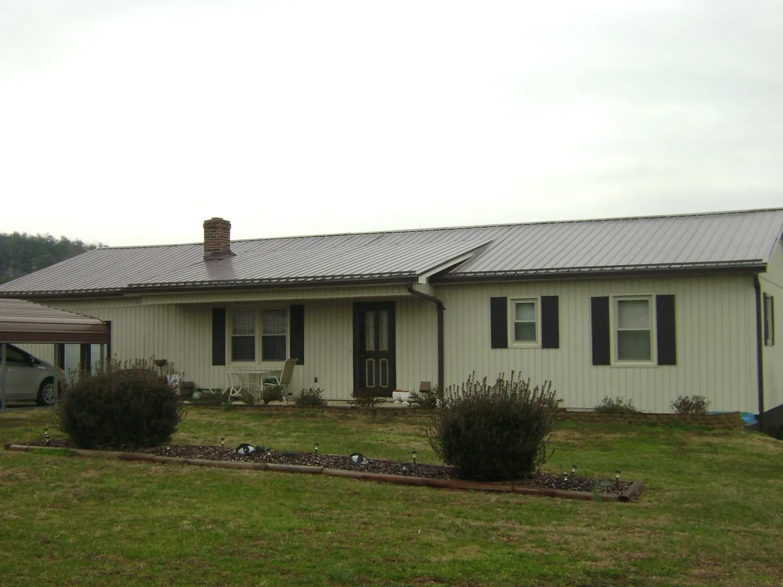 Brown metal roof on a cream sided ranch home with a brick chimney in Paris